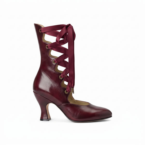 A single high-heeled ankle boot in glossy burgundy leather with matching satin laces threaded through cutout details, shown in profile against a plain white background.