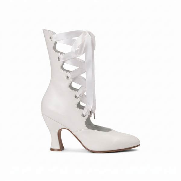 A white leather ankle boot with a mid-height kitten heel, featuring decorative cutouts on the shaft and white satin laces tied in a bow, shown against a plain white background.